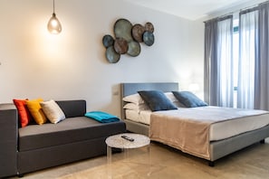 A modern bedroom with a bed, a sofa, a small round table, and a wall art piece.
