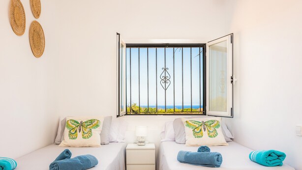 Una habitación con dos camas, una ventana con vistas y una mesita de noche con lámpara.