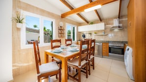Un comedor con una mesa y sillas de madera, una cocina con electrodomésticos, y una vista a través del ventanal.