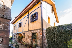 Un bâtiment à deux étages, doté de murs en pierre et d’une façade jaune, avec de nombreuses fenêtres et un petit jardin agrémenté de plantes en pot.