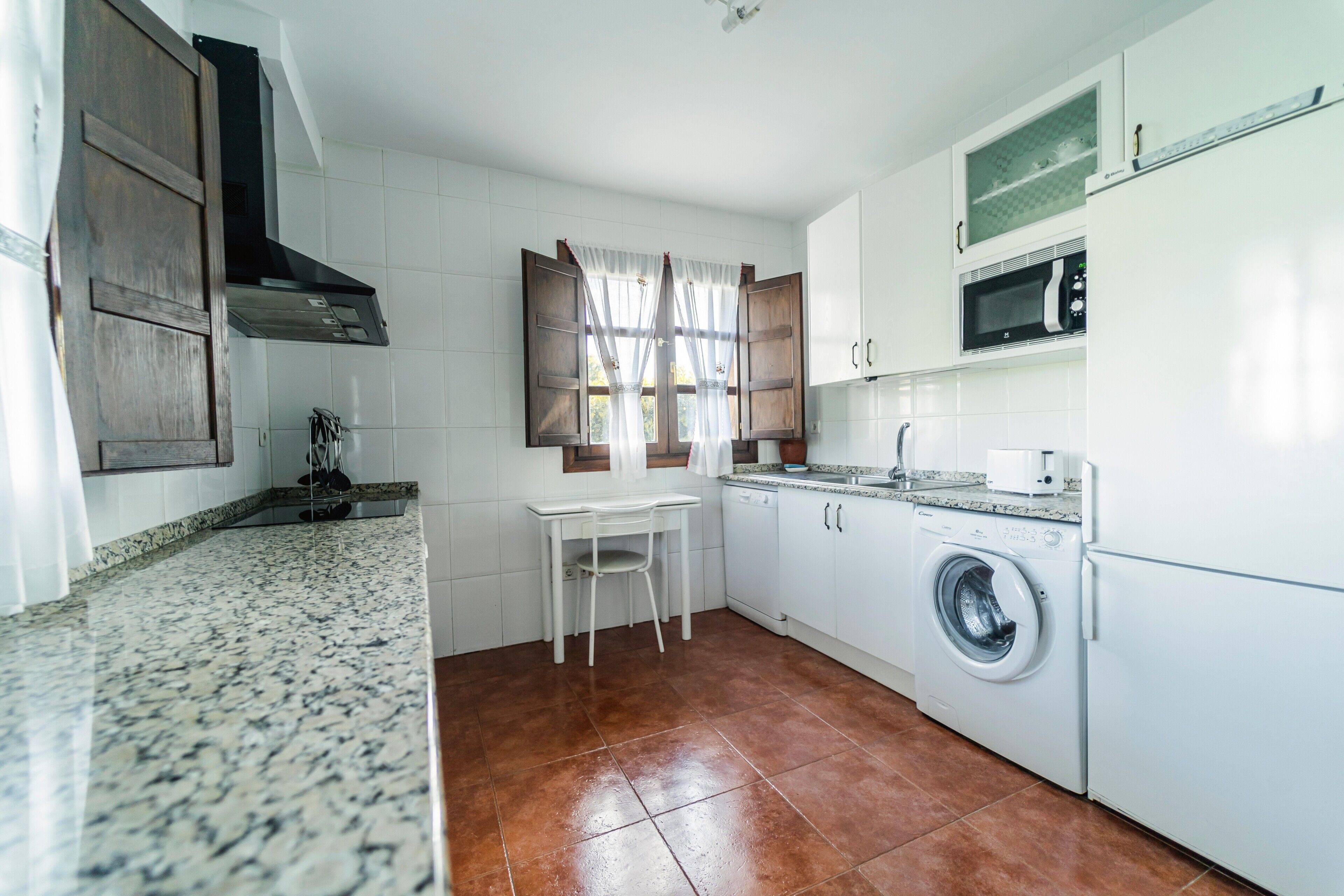 A kitchen with white cabinets, a washing machine, a microwave, and a window with curtains.