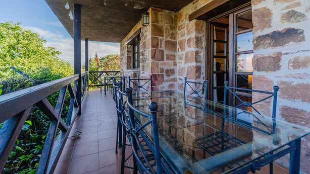 Un edificio de piedra con un patio cubierto, barandillas de metal y una baranda de vidrio con vistas a zonas verdes.