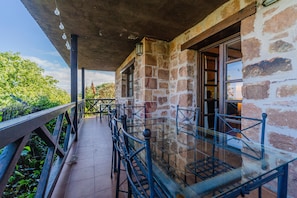 Un bâtiment en pierre doté d’un patio couvert, de rampes en métal et d’une balustrade en verre donnant sur un espace verdoyant.