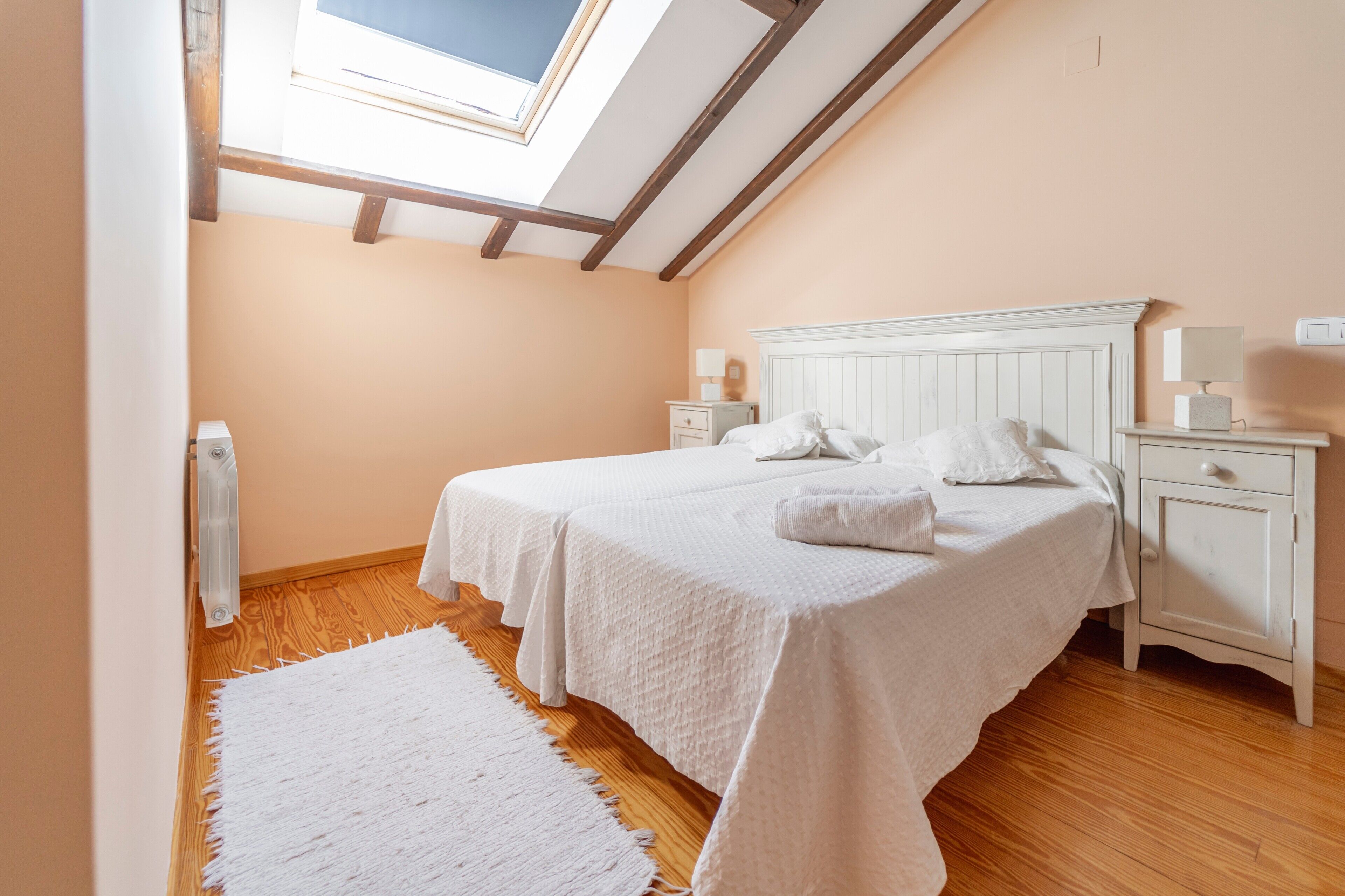 A bedroom with a skylight, a bed with white bedding, a nightstand, and a wooden floor.