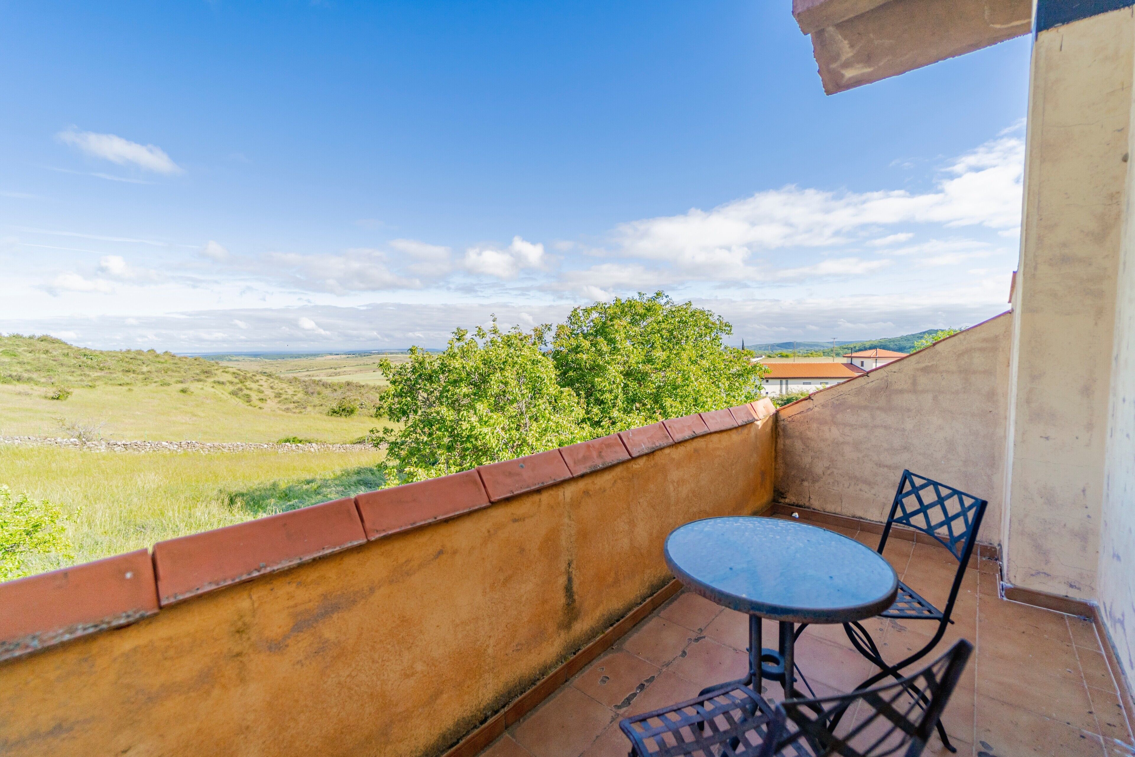 Un balcone con tavolo e sedie, affacciato su un paesaggio verde e dolci colline lontane.