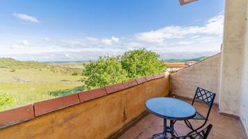 Un balcone con tavolo e sedie, affacciato su un paesaggio verde e dolci colline lontane.