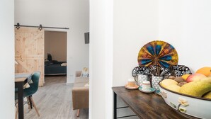 A room with a wooden door, a dining area with a table and chairs, a sofa, and a decorative bowl of fruit on a wooden table. - Apartment 'S' Istancu Vetzu' with Mountain View, Wi-Fi and Air Conditioning (Irgoli)
