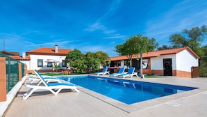 A swimming pool with lounge chairs, a tiled deck, and a building with a red roof.