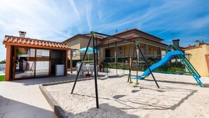 A playground with a slide and swings, a covered seating area, and a building with a tiled roof.