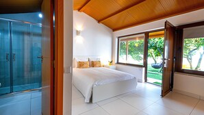 A bedroom with a bed, a glass shower enclosure, and a view of the outdoors.
