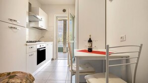 A modern kitchen with white cabinets, a dining table with a red placemat, and a bottle of wine. - Studio Apartment 'Tiny' with Shared Terrace and Wi-Fi (Brenzone)
