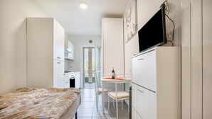 A compact hotel room with a bed, a small kitchenette, a desk with a chair, and a TV mounted on the wall. - Studio Apartment 'Tiny' with Shared Terrace and Wi-Fi (Brenzone)