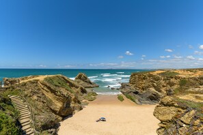 Une plage au sol rocheux, un ciel dégagé et une personne allongée sur le sable.