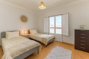 Une chambre avec deux lits, une commode, un tapis à motifs, un élément décoratif mural et une fenêtre donnant sur un paysage agréable.