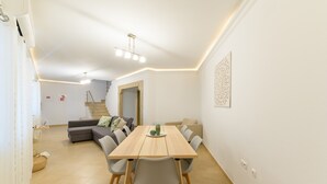 Ein modernes Wohnzimmer mit Esstisch, grauem Sofa und einer Treppe, die in einen oberen Bereich führt.