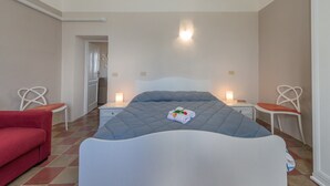 A hotel room with a bed, two nightstands, a red sofa, and two white chairs.