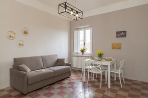 A living room with a sofa, dining table, chairs, and a window with a view.