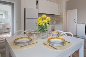 A dining table set with plates, cutlery, and a vase of flowers in a modern kitchen with white cabinetry and a tiled backsplash.