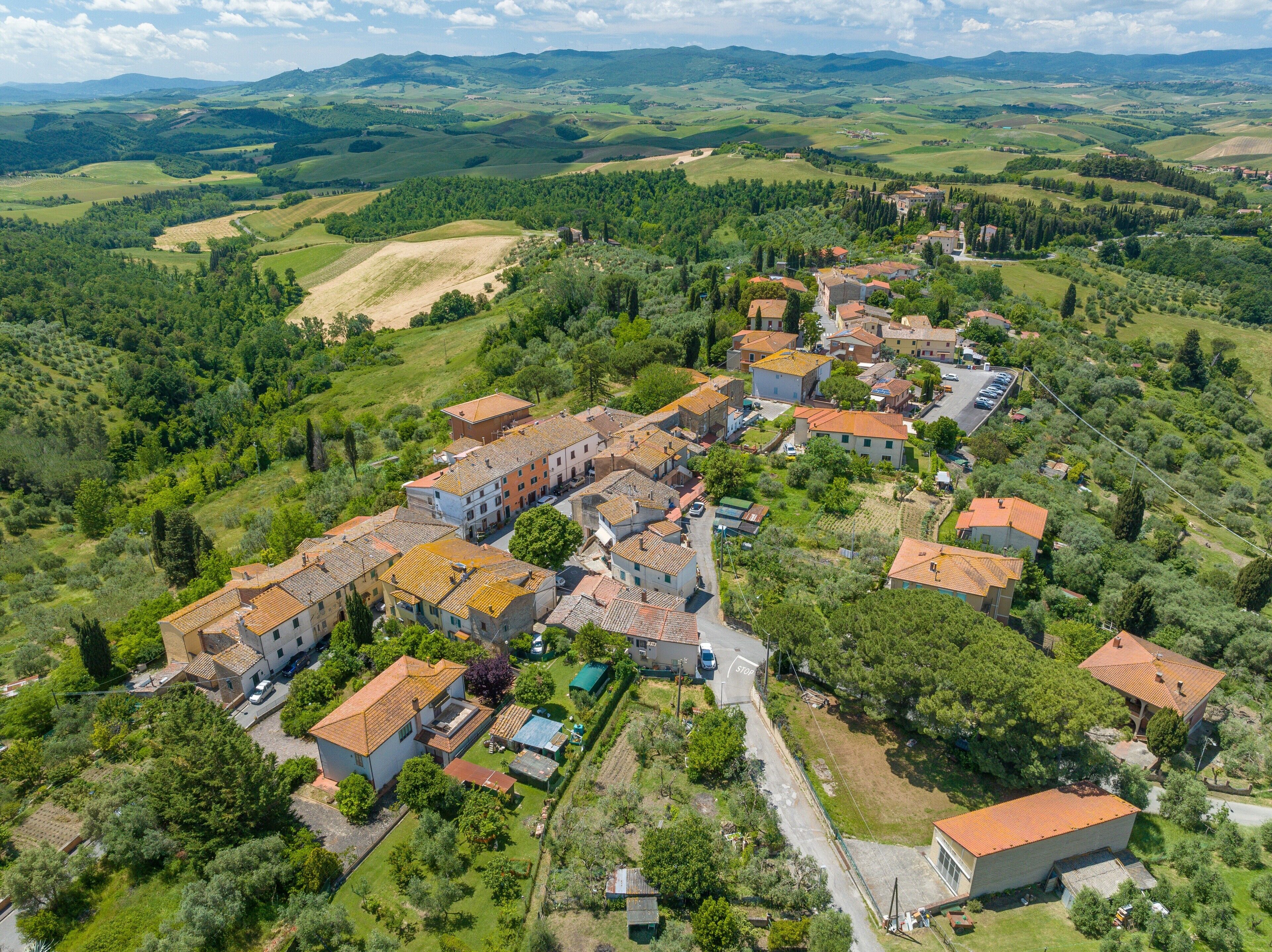 Une vue aérienne d’un village à l’architecture traditionnelle, entouré d’une végétation luxuriante et de collines ondulantes.