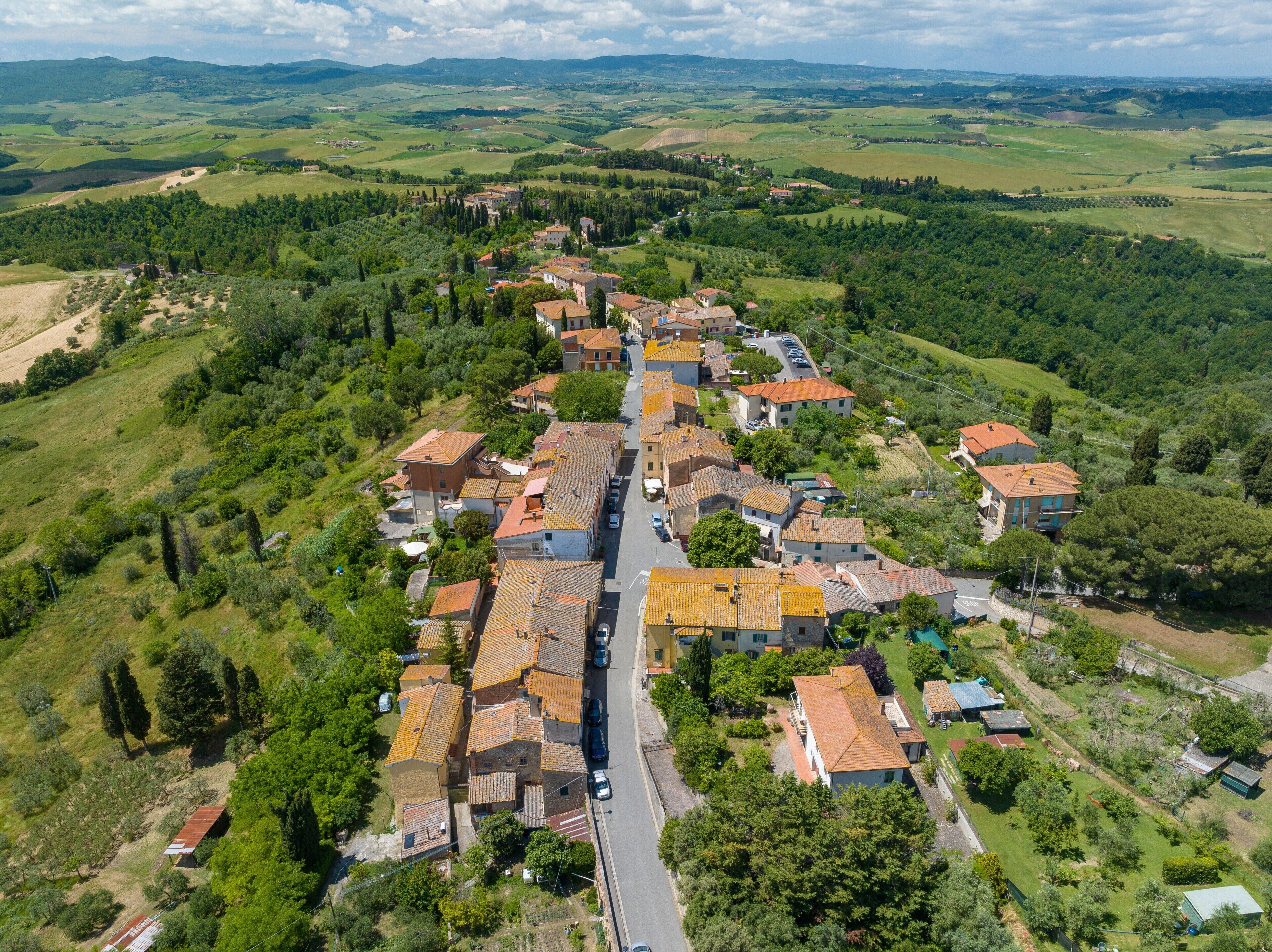An aerial view of a village with terraced houses, a central road, and surrounding green hills.