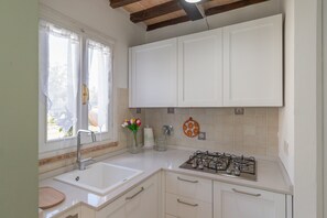 A kitchen with white cabinets, a gas stove, a sink, and a window with curtains.
