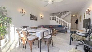 Een eethoek met een tafel, stoelen, een bank, een trap en een televisie.