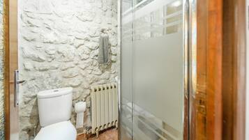 A bathroom with a stone wall, a toilet, a radiator, and a glass shower enclosure.