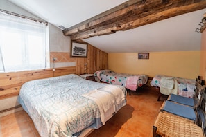 Quarto com uma cama grande, duas camas menores, teto de madeira e uma janela com cortina.