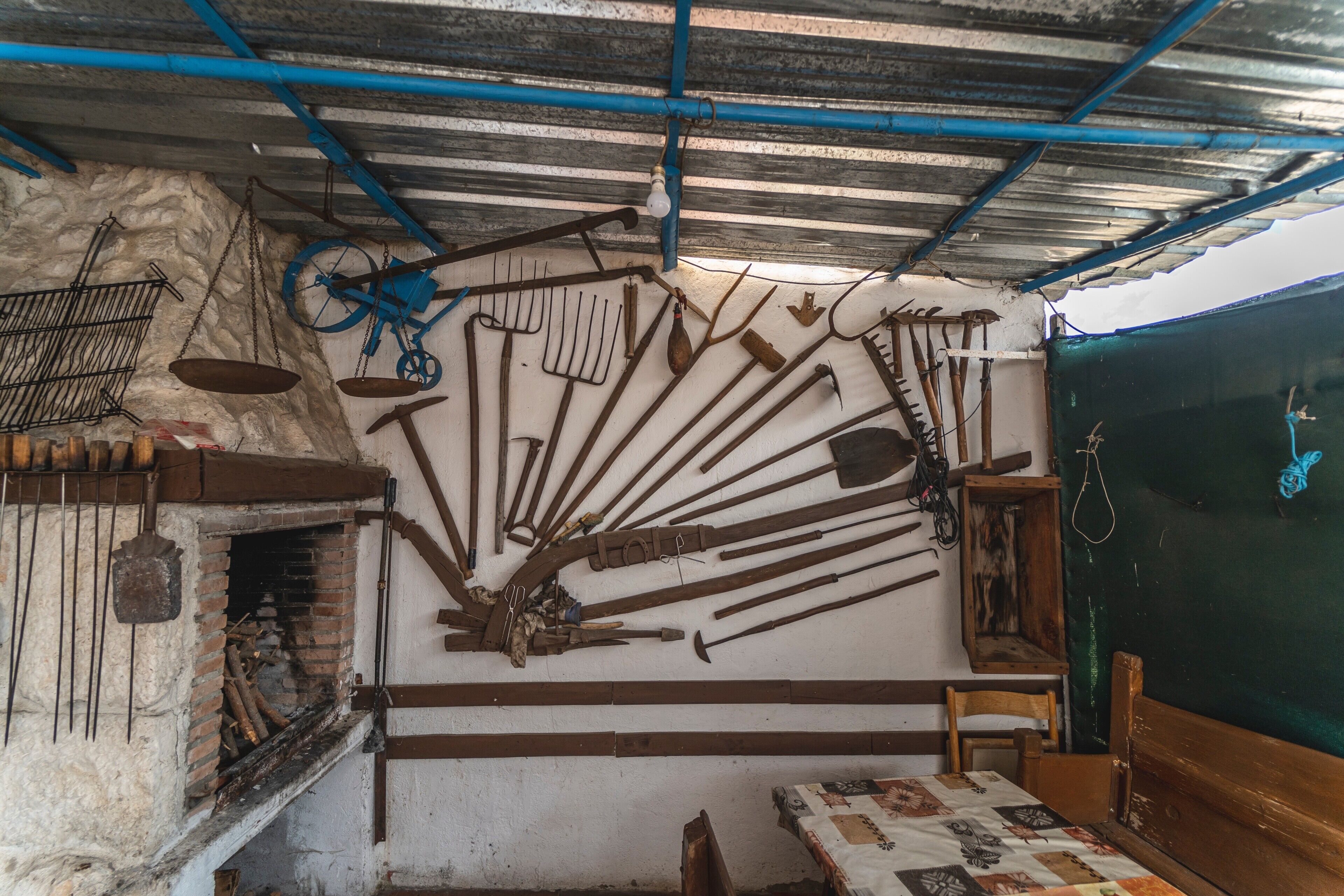 Una habitación rústica con chimenea de ladrillo, muebles de madera y diversas herramientas colgadas en la pared.