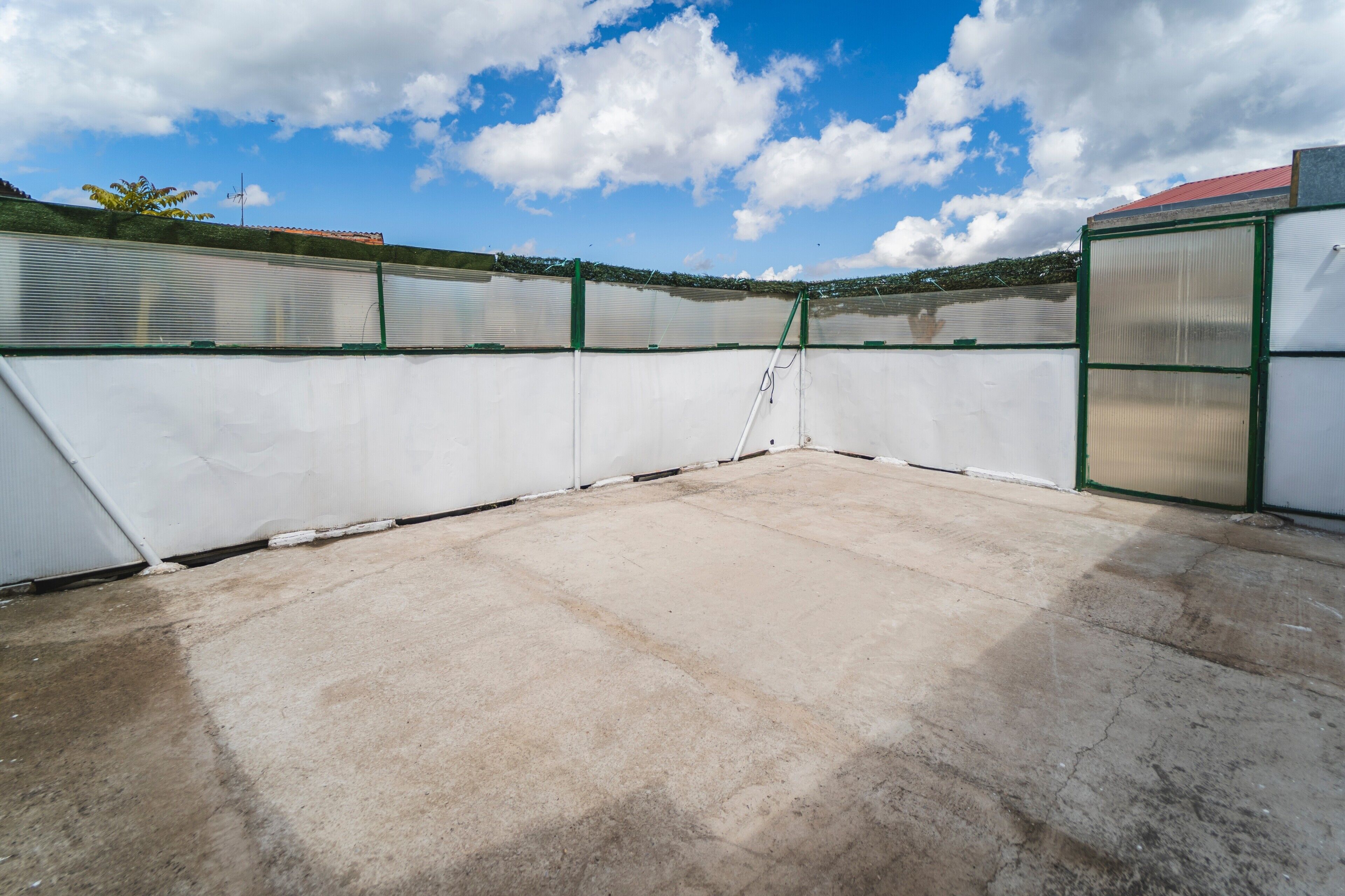 A rooftop with a concrete floor, metal fencing, and a ladder.