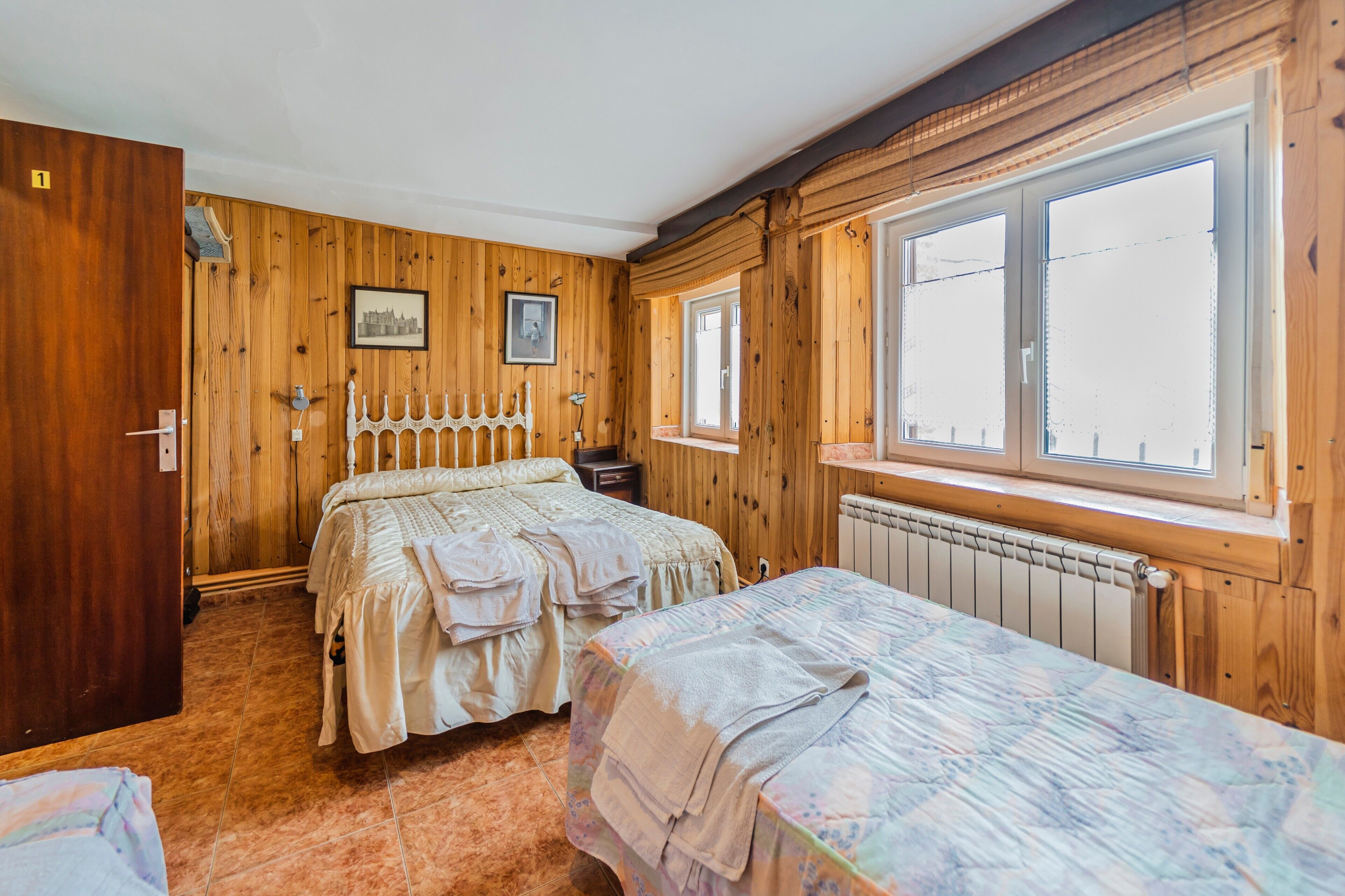 Ein Zimmer mit Holzwänden, einem Bett, einem zusätzlichen Bett, einem Heizkörper und einem Fenster.