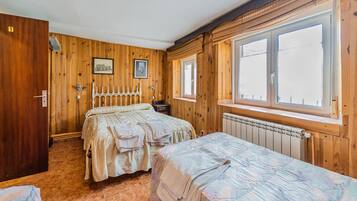 Ein Zimmer mit Holzwänden, einem Bett, einem zusätzlichen Bett, einem Heizkörper und einem Fenster.