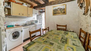 A compact kitchen with a washing machine, wooden cabinets, a microwave, and a table with a patterned tablecloth.