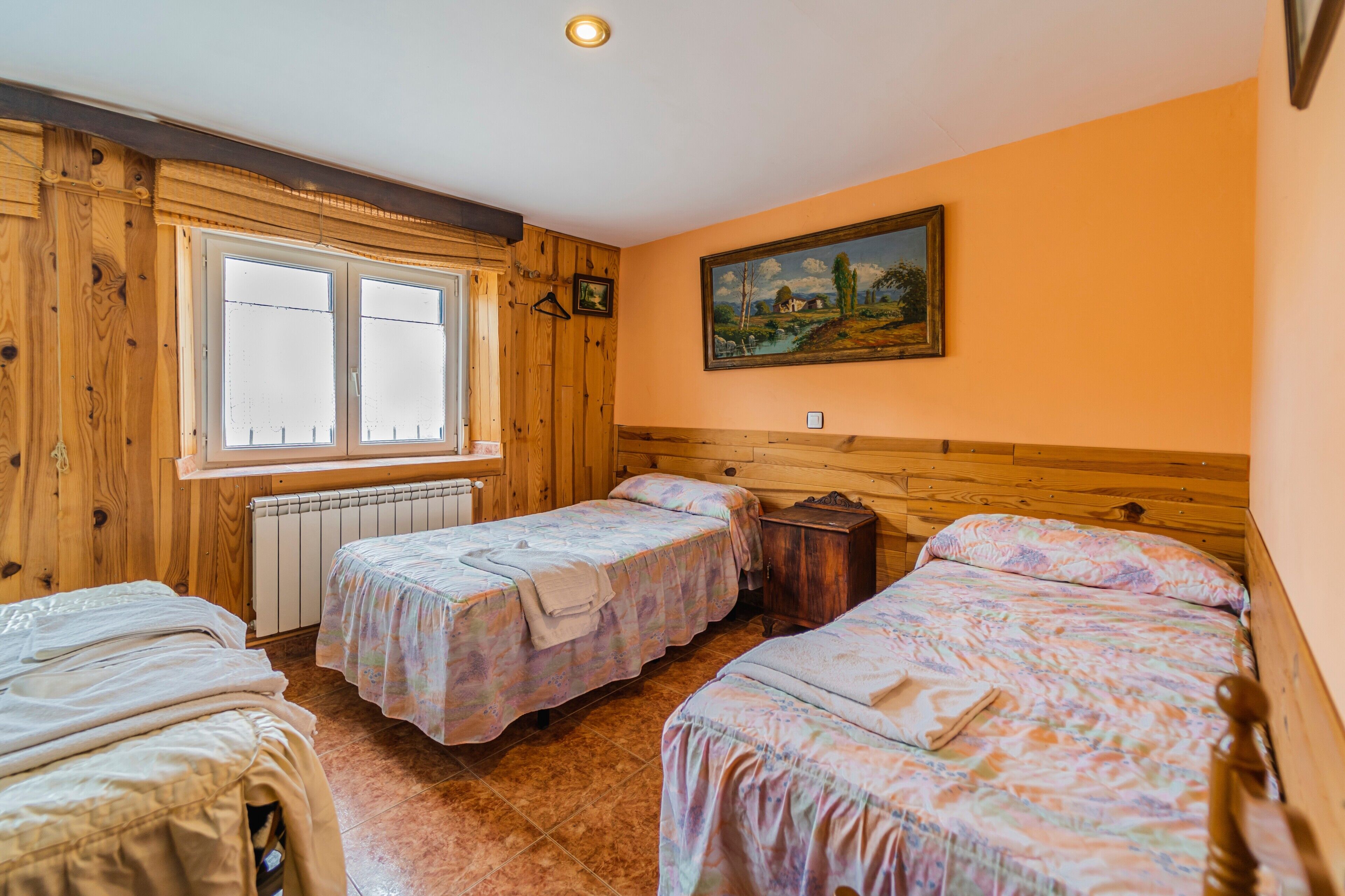 A room with two beds, a window, a radiator, and a painting on the wall.