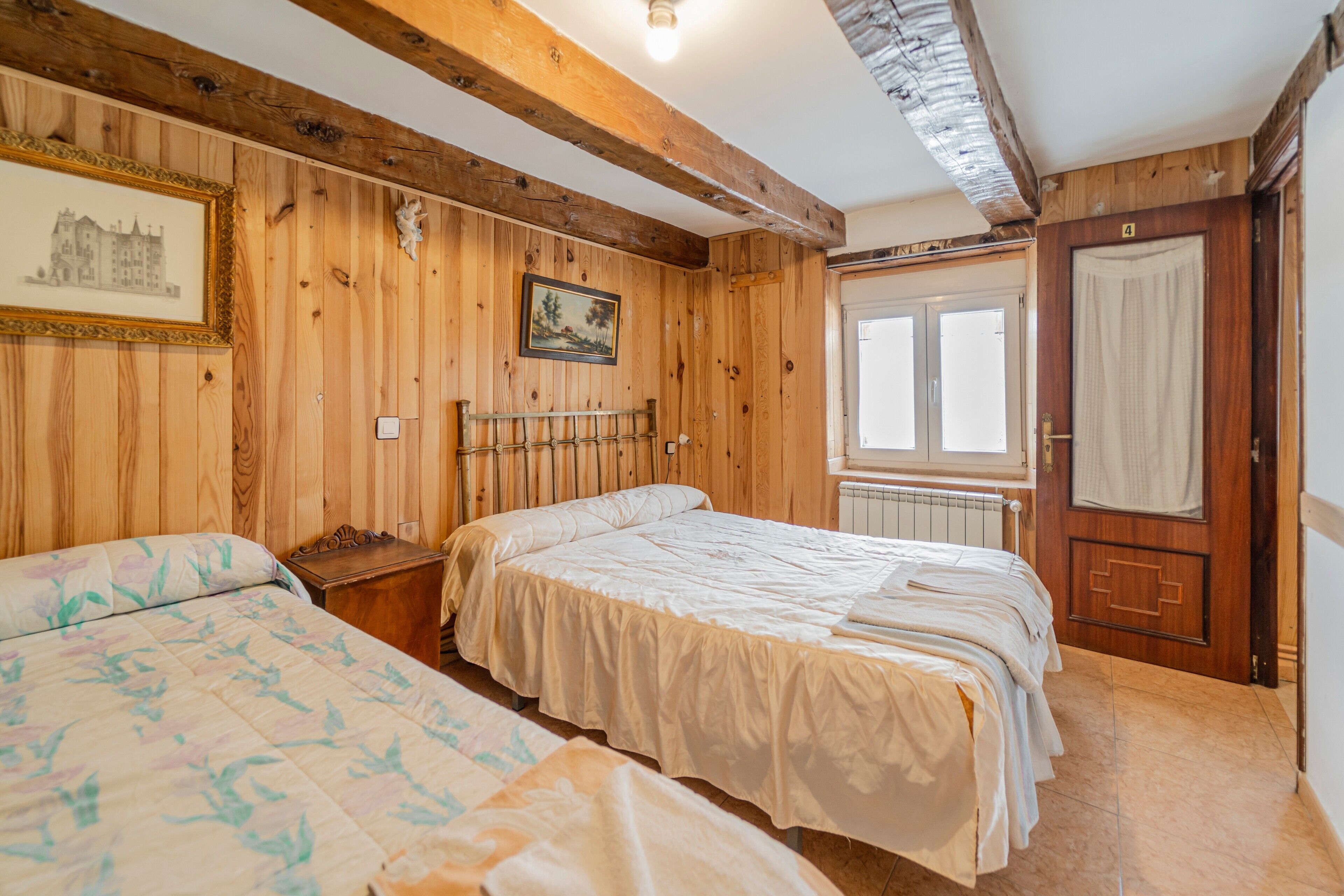 A room with wooden paneling, two beds, a radiator, a window, and a door.