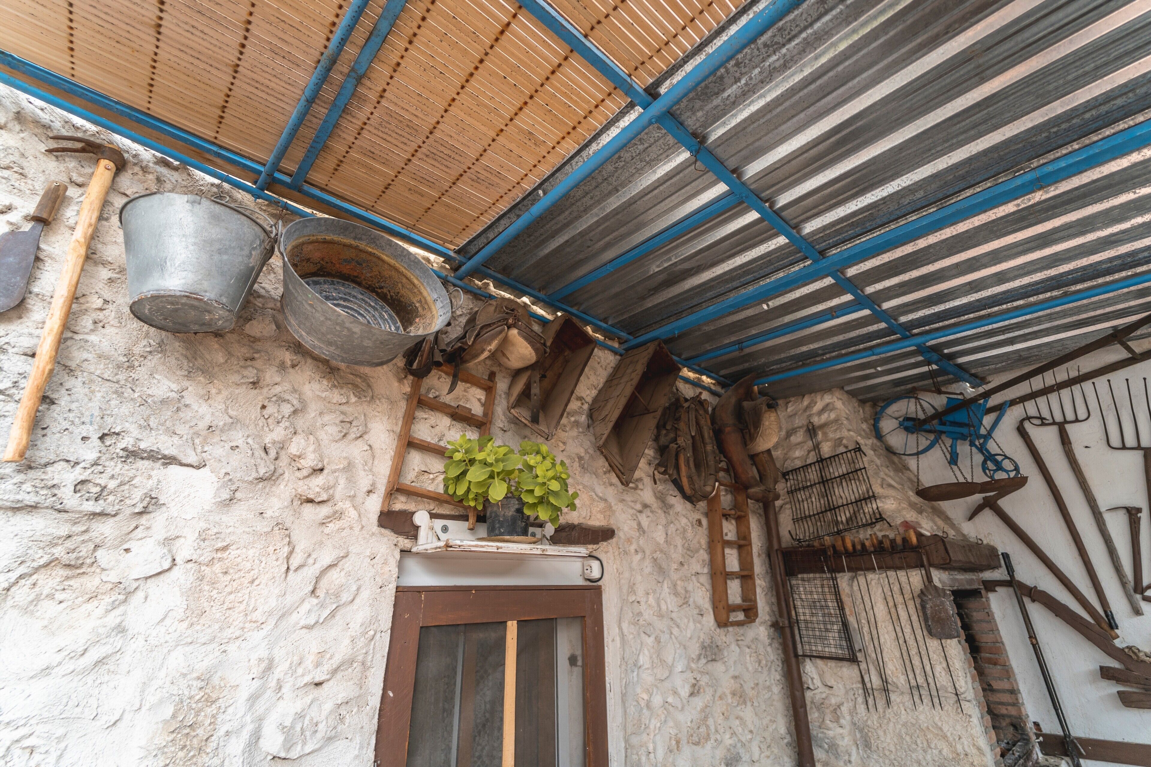 Um edifício rústico com telhado de metal corrugado, uma porta de madeira e diversas ferramentas e equipamentos pendurados nas paredes.