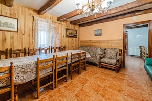 Uma sala de jantar com uma mesa comprida, cadeiras de madeira, um sofá estampado e um candelabro.