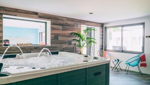 A modern spa area with a hot tub, wooden wall decor, a potted plant, and a view of the outside.