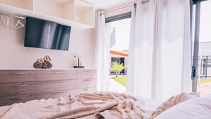 A bedroom with a bed, a TV mounted on the wall, a dresser, and a view of the outdoors.