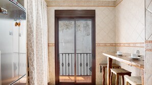 Eine Küche mit einem Kühlschrank, einem Holztisch mit Hocker und einer Glastür zum Balkon.