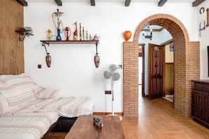 A room with a sofa, a fan, a table, a brick fireplace, and a wooden ceiling. - Villa Canijo Barbate – Beach House with Private Terrace (Barbate)