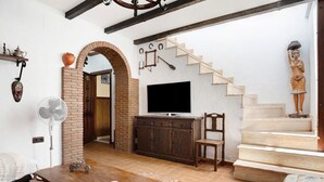 Ein Wohnzimmer mit Fernseher, Holzmöbeln, einem Ventilator und einer Treppe.