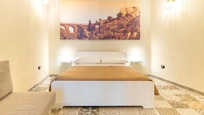 Quarto com cama, sofá, uma imagem grande presa na parede e duas luminárias fixadas na parede.