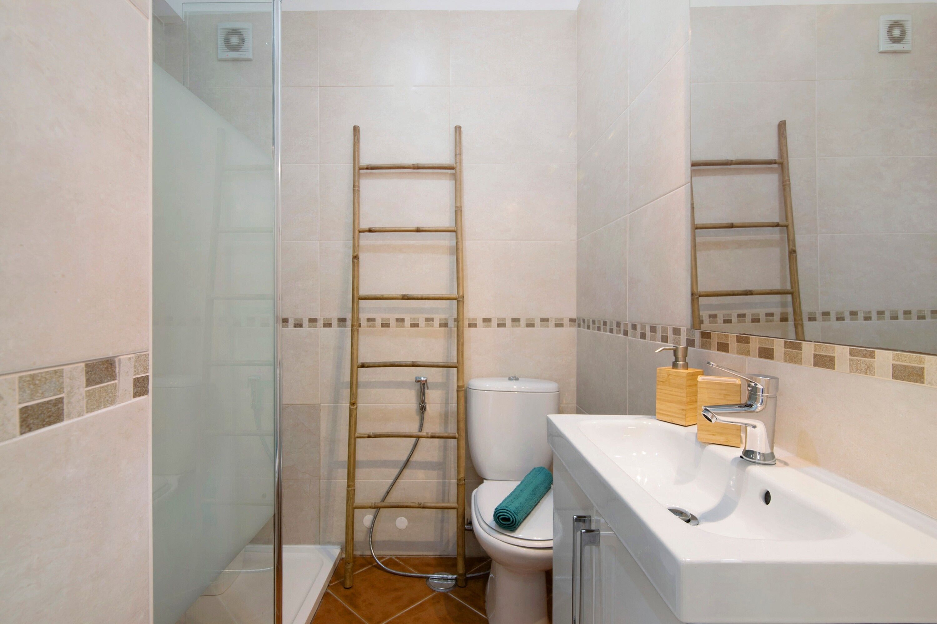Un bagno con cabina doccia in vetro, un water, un lavandino con specchio e una scala di legno appoggiata al muro.