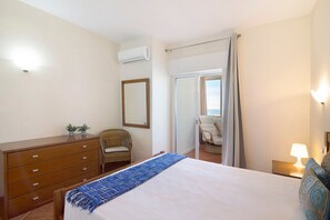 Une chambre à coucher comprenant un lit, une commode, une chaise, un miroir et un appareil de climatisation.