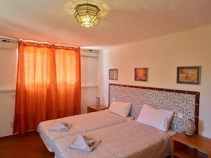 Une chambre à coucher avec une couvre-lit à motifs, une tête de lit ornée d’un décor, une table de chevet avec un vase et un luminaire fixé au mur.