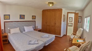 A bedroom with a large bed, a wardrobe, a desk with a chair, and a window.