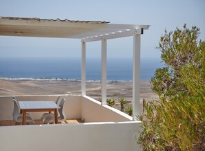 A covered outdoor seating area with a table and chairs, overlooking a coastal landscape.