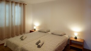 Een slaapkamer met een bed, twee nachtkastjes met lampen, een raam met gordijnen en een plafondlamp.