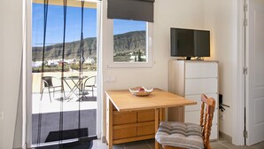 A room with a wooden table, a TV on a cabinet, a chair, and a view of a mountainous landscape through a window. - Vacation Apartment 'Fewo Arafo' with Sea View, Private Terrace and Wi-Fi (Güímar)